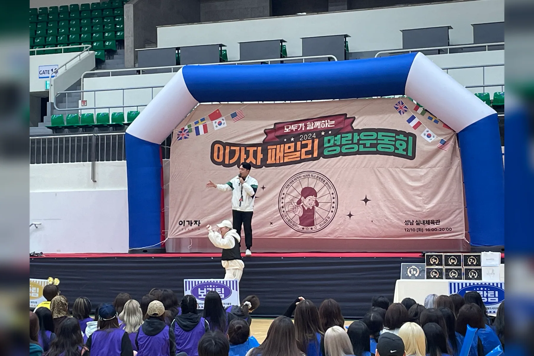 실내 체육대회 무대에서 전문 MC가 많은 참가자에게 오프닝을 진행하는 실제 현장