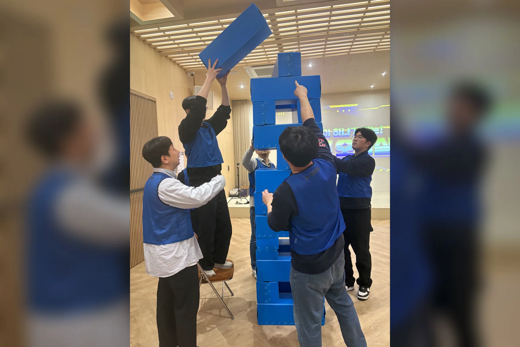 파란 팀 참가자들이 사람 키보다 높은 대형 젠가를 함께 쌓는 실제 경기